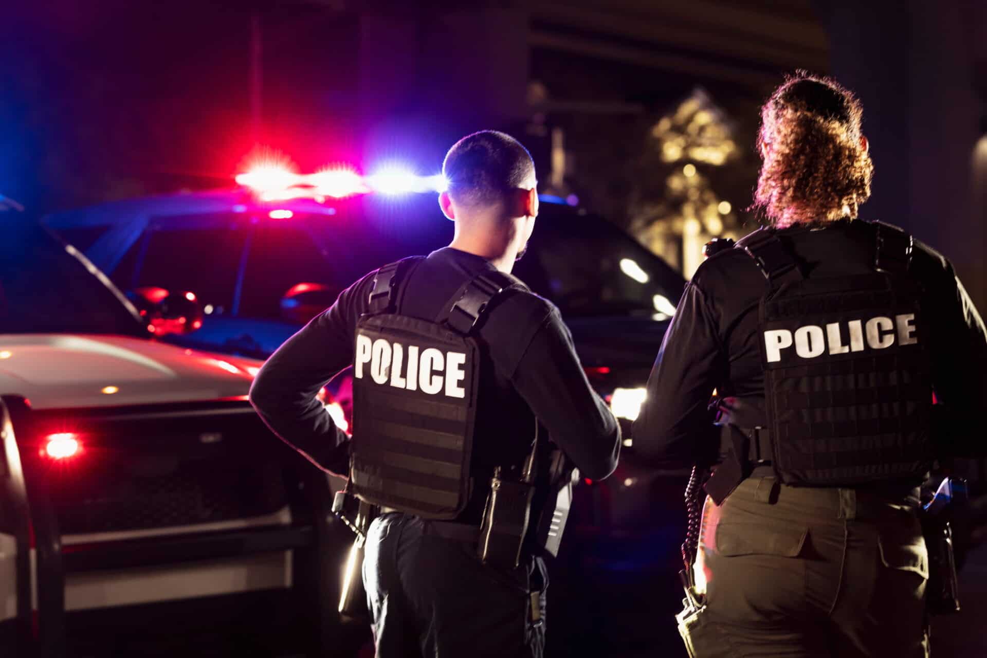 male and female police officers overlooking a scene with police lights in the background at night